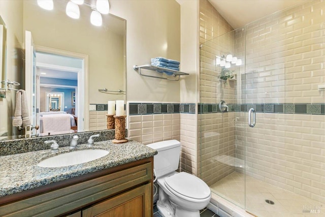 ensuite bathroom with vanity, a wainscoted wall, a stall shower, tile walls, and toilet