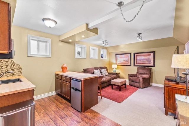 kitchen featuring a sink, tasteful backsplash, a peninsula, light countertops, and dark wood-style flooring