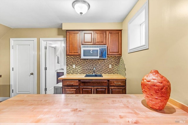 kitchen featuring stainless steel microwave, backsplash, light countertops, brown cabinets, and a sink