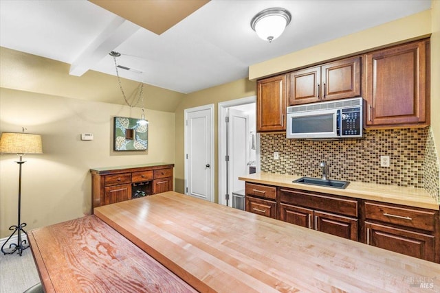 kitchen with a sink, stainless steel microwave, wood counters, tasteful backsplash, and vaulted ceiling with beams