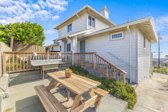 back of property with outdoor dining space, a deck, a patio, fence, and a chimney