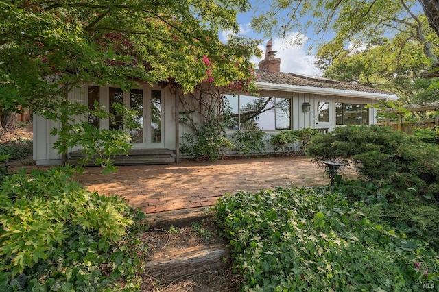 rear view of house featuring french doors, a chimney, and board and batten siding