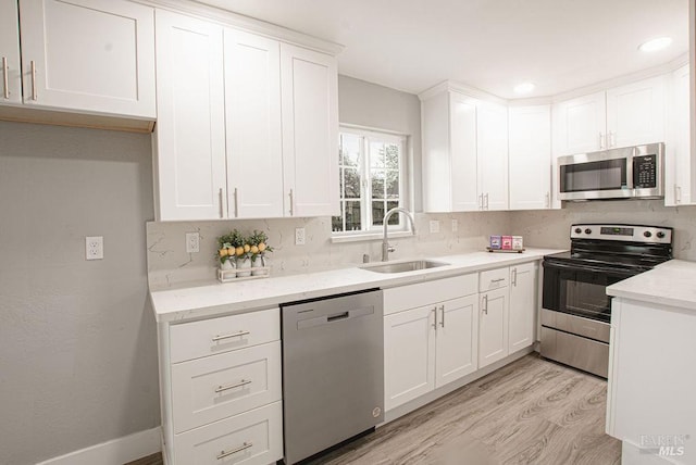 kitchen featuring a sink, tasteful backsplash, white cabinetry, stainless steel appliances, and light wood finished floors