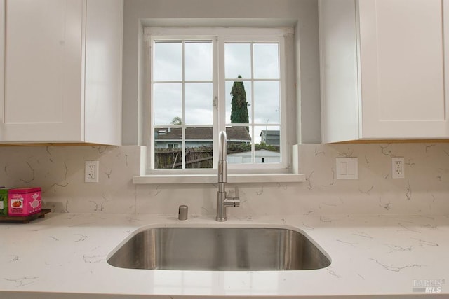 kitchen with a sink, light stone countertops, tasteful backsplash, and white cabinets