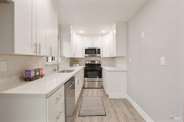 kitchen with a sink, appliances with stainless steel finishes, white cabinets, light wood finished floors, and light countertops