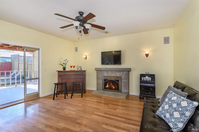 living area featuring a fireplace, wood finished floors, baseboards, and a ceiling fan