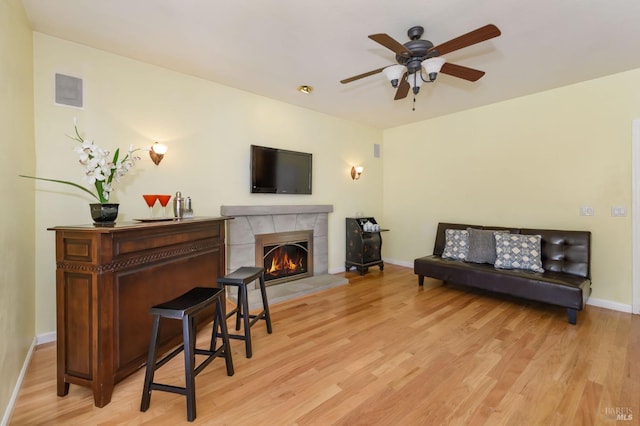 living room featuring baseboards, a ceiling fan, light wood-style flooring, and a fireplace