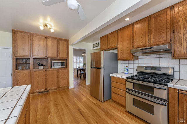 kitchen featuring under cabinet range hood, stainless steel appliances, light wood-style floors, and tile counters