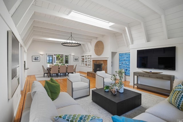 living area featuring lofted ceiling with skylight, a notable chandelier, a fireplace with raised hearth, wood finished floors, and baseboards