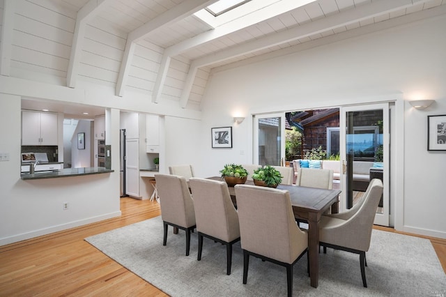 dining room with vaulted ceiling with skylight, baseboards, and light wood finished floors