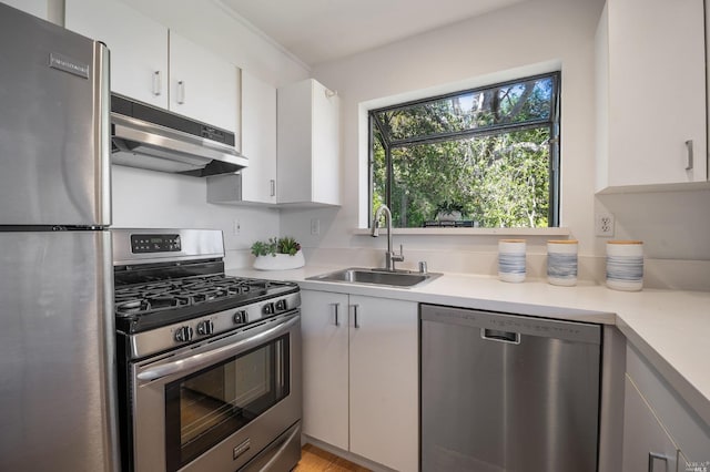 kitchen featuring under cabinet range hood, light countertops, appliances with stainless steel finishes, white cabinetry, and a sink