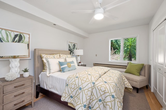 bedroom with a baseboard heating unit, wood finished floors, a closet, and a ceiling fan