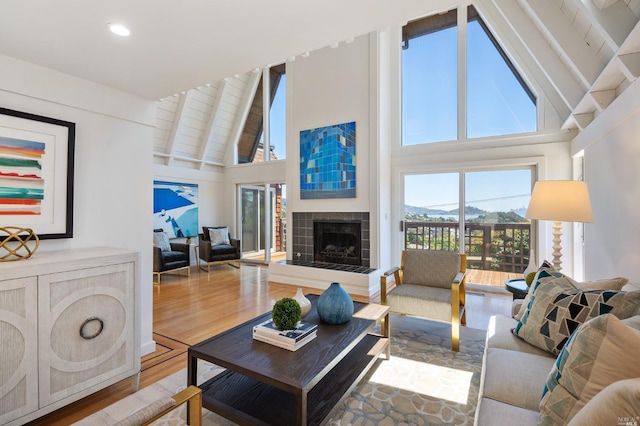 living area featuring wood finished floors, high vaulted ceiling, beam ceiling, recessed lighting, and a tile fireplace