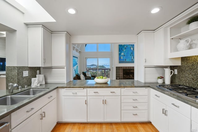 kitchen featuring white cabinets, a tile fireplace, light wood-style flooring, and a sink