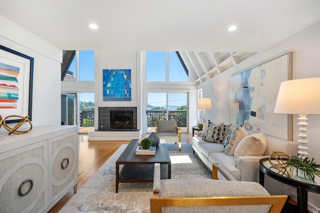 living area with a wealth of natural light, light wood finished floors, high vaulted ceiling, and a tile fireplace