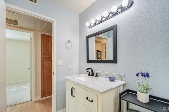 bathroom with a textured wall, vanity, baseboards, and wood finished floors