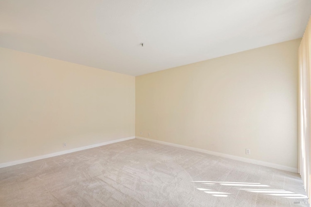 unfurnished room featuring baseboards and light carpet