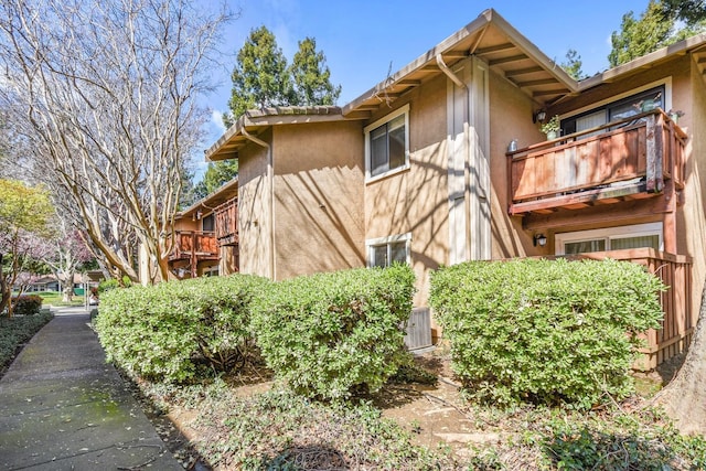 view of side of property with a tile roof, stucco siding, central AC, and a balcony