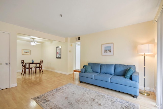 living area featuring baseboards, visible vents, a ceiling fan, and light wood-style floors