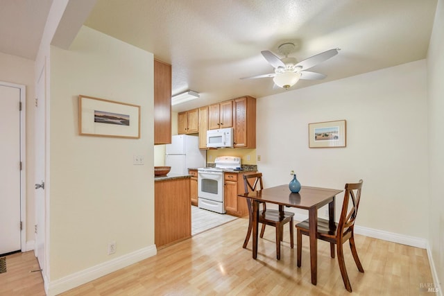 kitchen with white appliances, light wood-style floors, dark countertops, and a ceiling fan