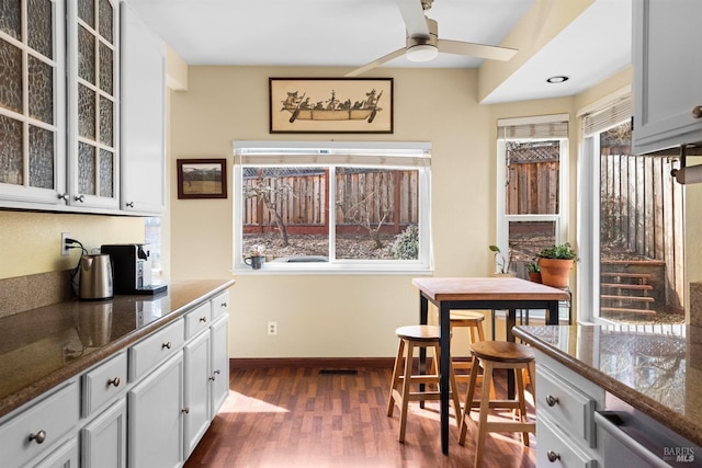 kitchen featuring dark wood-style floors, visible vents, baseboards, ceiling fan, and glass insert cabinets