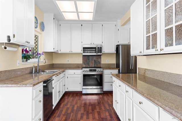 kitchen featuring dark wood-type flooring, light stone counters, stainless steel appliances, white cabinetry, and a sink