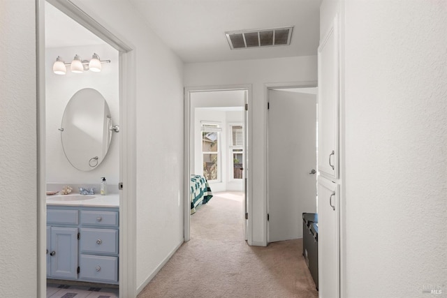 hall featuring a sink, visible vents, and light colored carpet