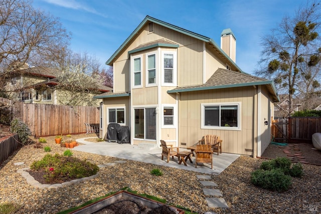 back of house with a shingled roof, a patio area, a fenced backyard, and a chimney