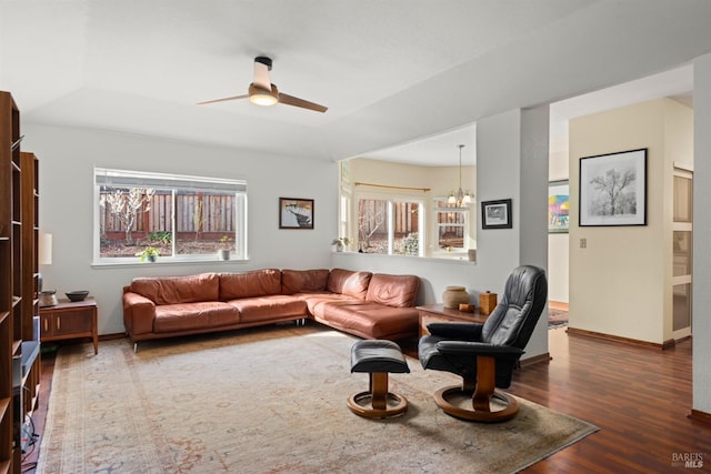 living room featuring wood finished floors, ceiling fan with notable chandelier, and baseboards