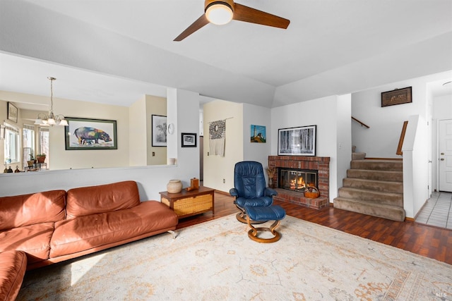 living area with ceiling fan with notable chandelier, wood finished floors, a fireplace, lofted ceiling, and stairs