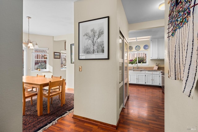 corridor with baseboards, dark wood-style flooring, a chandelier, and a sink