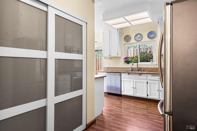 kitchen with light stone counters, appliances with stainless steel finishes, dark wood-style floors, white cabinetry, and a sink