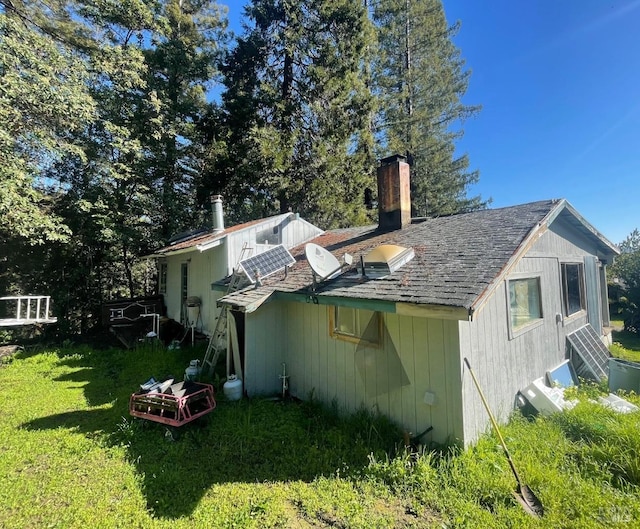 view of side of home with roof with shingles, a chimney, and a lawn