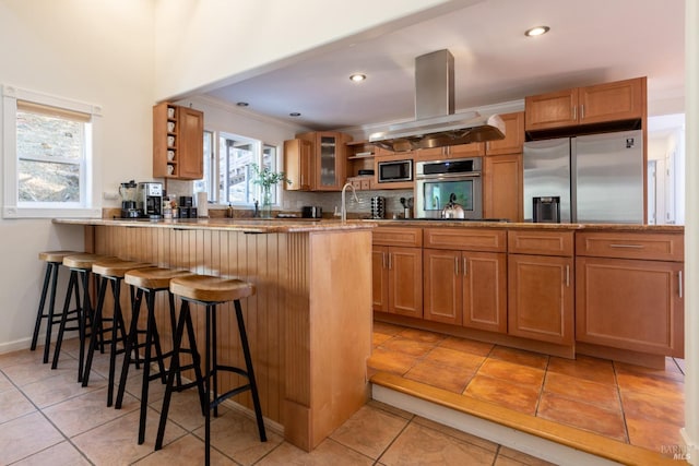 kitchen featuring backsplash, built in appliances, a breakfast bar area, a peninsula, and island range hood