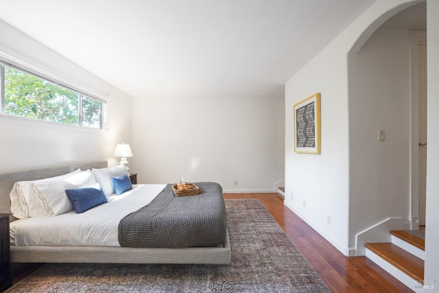 bedroom with baseboards, arched walkways, and dark wood finished floors