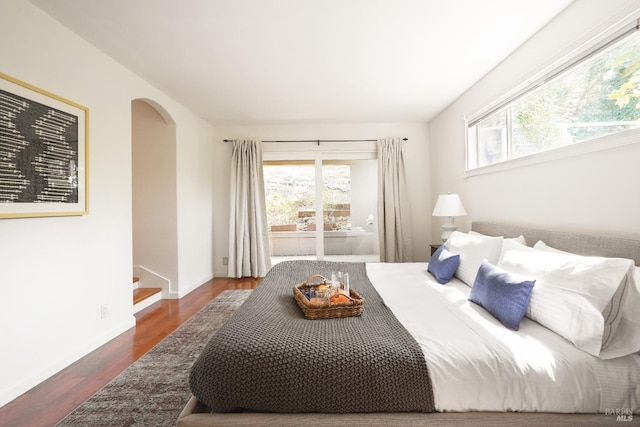 bedroom featuring multiple windows, arched walkways, baseboards, and wood finished floors