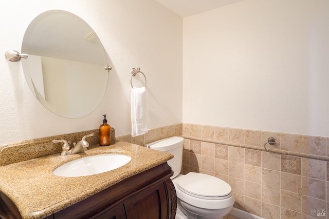 bathroom with wainscoting, toilet, tile walls, and vanity