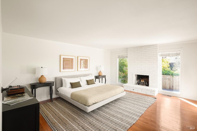 bedroom featuring wood finished floors, visible vents, a fireplace, ornamental molding, and access to outside