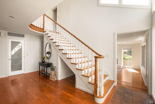 stairway featuring a high ceiling, baseboards, visible vents, and wood-type flooring