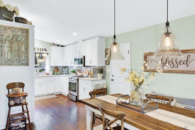 kitchen with light countertops, decorative backsplash, appliances with stainless steel finishes, white cabinetry, and dark wood-style flooring