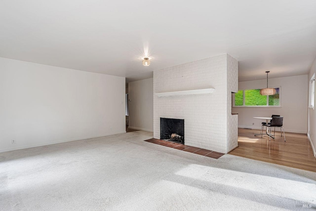 unfurnished living room featuring baseboards, carpet, a brick fireplace, and wood finished floors