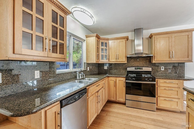 kitchen with light brown cabinetry, stainless steel appliances, wall chimney range hood, and a sink