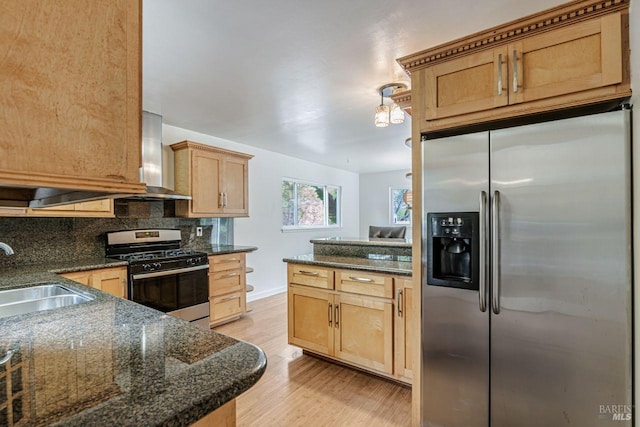 kitchen featuring wall chimney range hood, decorative backsplash, light wood-style flooring, appliances with stainless steel finishes, and a sink