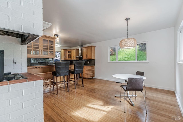 kitchen with brown cabinetry, light wood-style flooring, dark countertops, wall chimney range hood, and tasteful backsplash