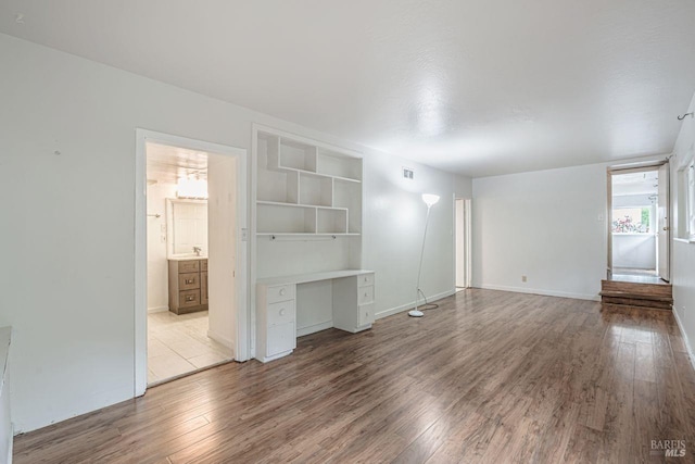 unfurnished living room with wood finished floors, baseboards, visible vents, built in study area, and a sink