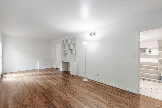 unfurnished living room featuring visible vents, baseboards, and wood finished floors