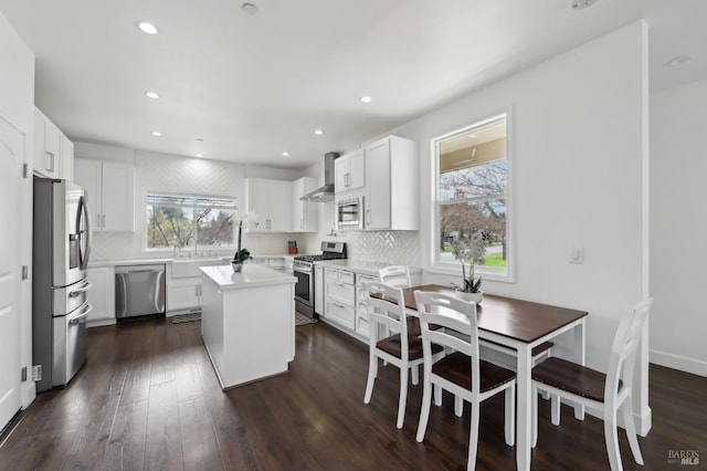 kitchen featuring wall chimney range hood, backsplash, a wealth of natural light, and stainless steel appliances