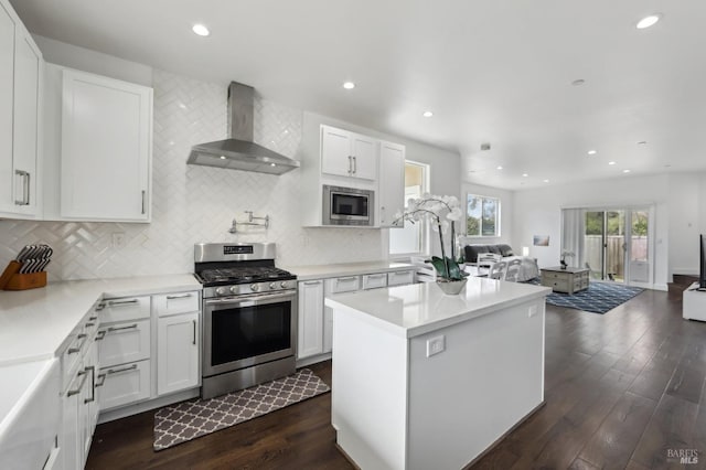 kitchen featuring dark wood-type flooring, appliances with stainless steel finishes, wall chimney exhaust hood, open floor plan, and a center island