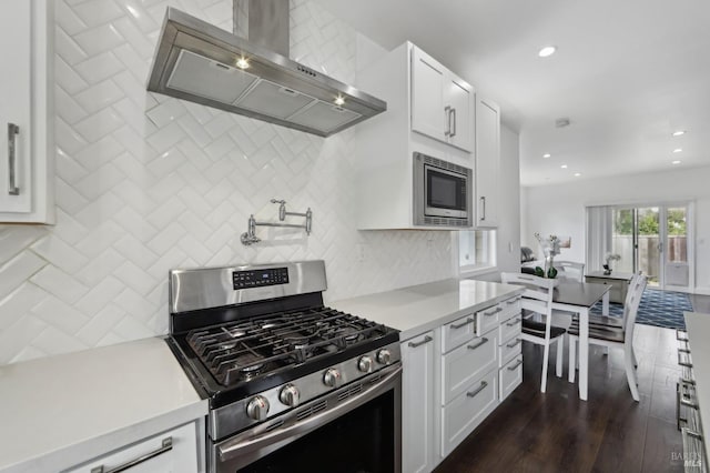 kitchen with backsplash, appliances with stainless steel finishes, wall chimney exhaust hood, light countertops, and dark wood-style flooring