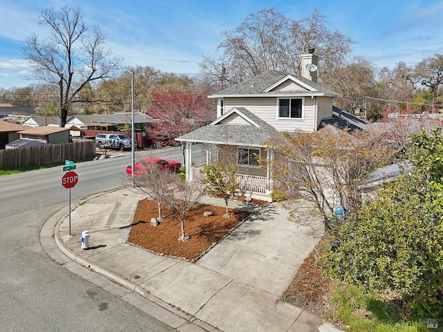 view of front of home with fence, driveway, roof with shingles, covered porch, and a chimney